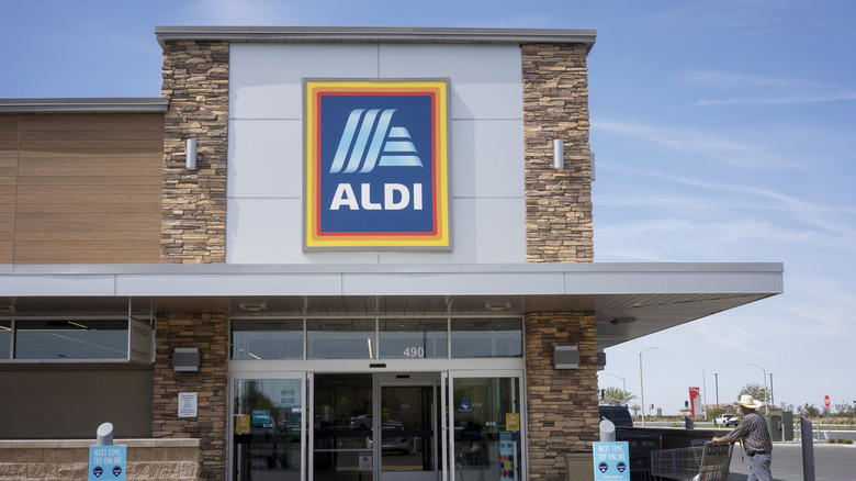 an Aldi store, viewed from the parking lot, with a person pushing a cart towards the door.