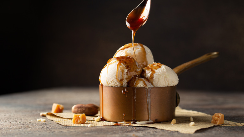 Vanilla ice cream being topped with caramel sauce.