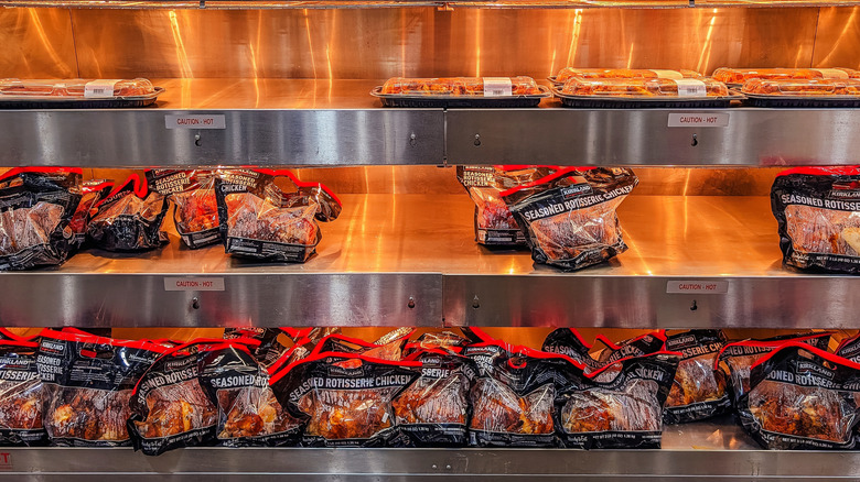 Shelves of cooked Costco rotisserie chickens in Costco store, with shelf of cooked food above it