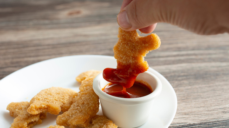 Hand dipping a dinosaur nugget into BBQ sauce