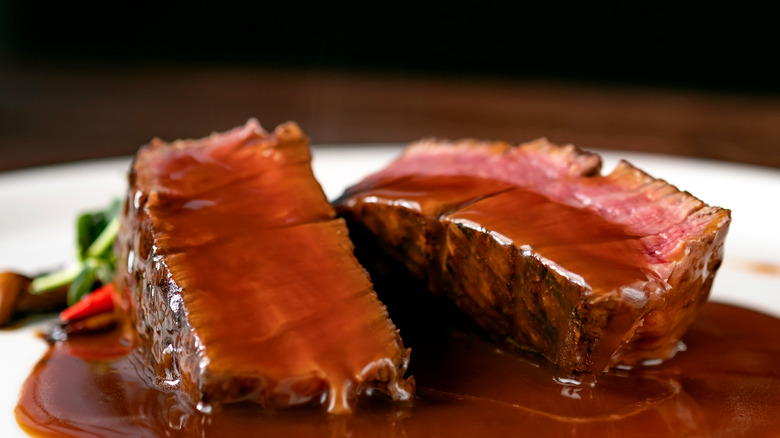 sliced steak sitting in demi-glace sauce