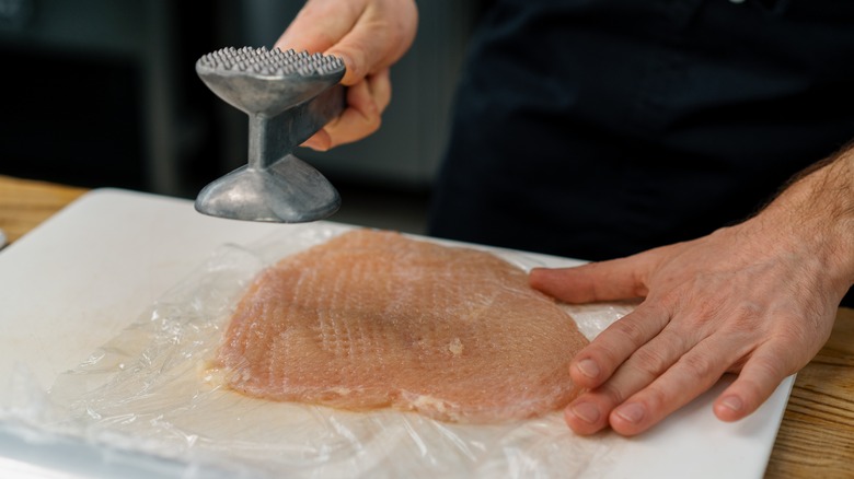 person tenderizing a chicken breast 