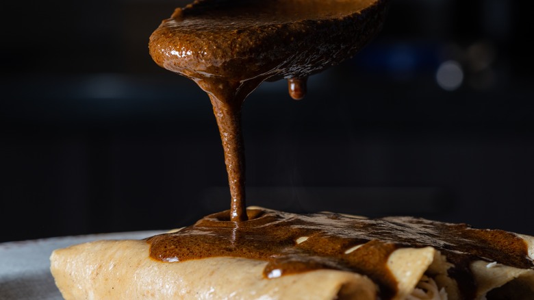 pouring brown mole sauce onto enchiladas