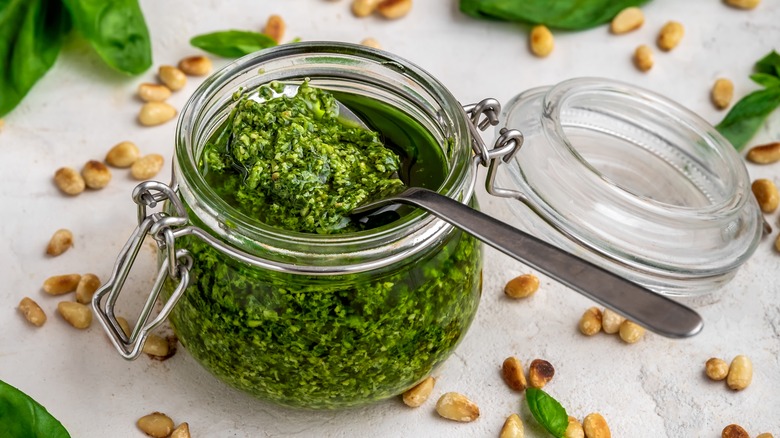 Green pesto in glass jar spoon nuts