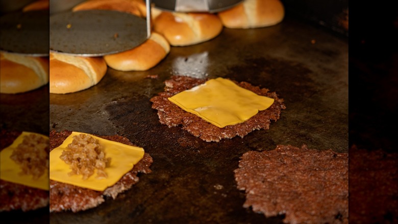 Smash burgers being cooked on a hot griddle