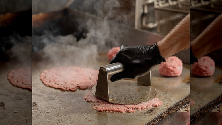 Metal burger press smashing burger patties on the griddle