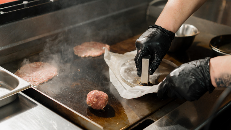 Chef pressing a smash burger using parchment paper