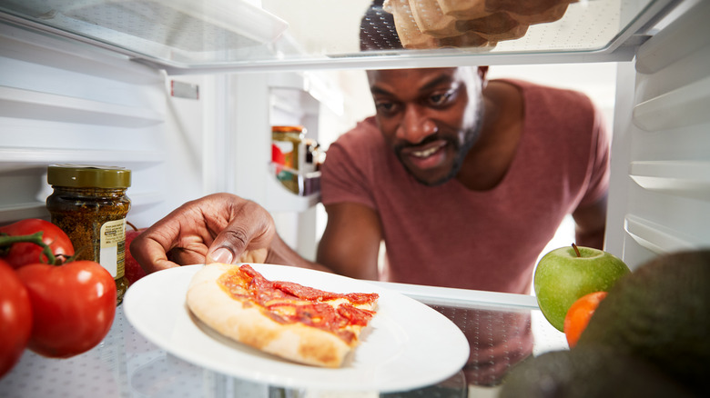 person taking pizza from refrigerator