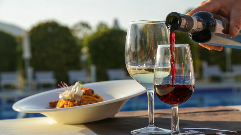 Bowl of pasta in the background, glasses of white and red wine in the foreground