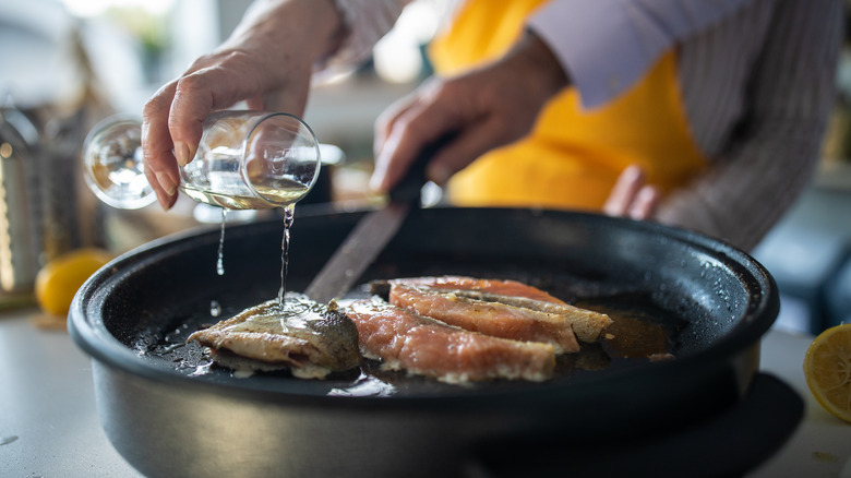 Person adding wine to pan