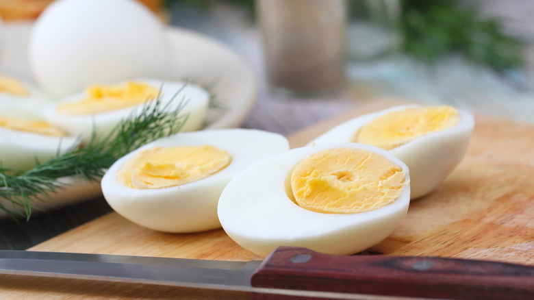 Halved hard-cooked eggs on a cutting board with a knife