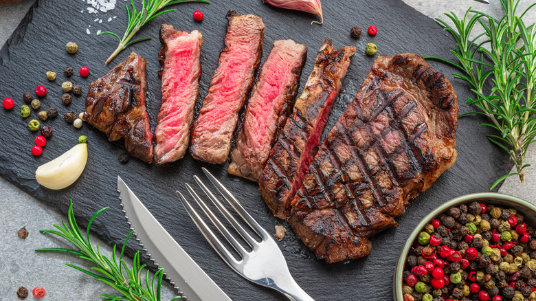 sliced ribeye steak on slate board with herbs and knife and fork