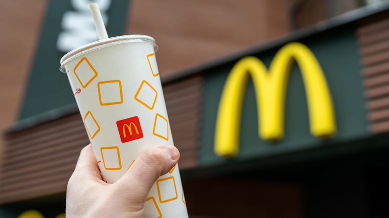 A person holds up a drink in front of McDonald's