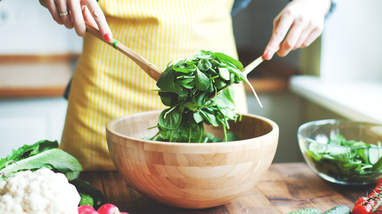 tossing salad in large wooden bowl