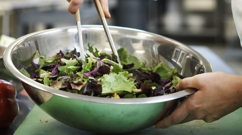 tongs tossing salad in bowl