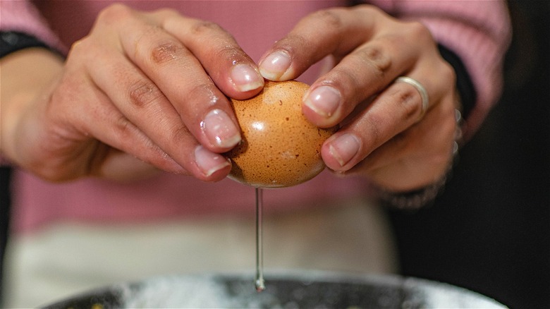 Hands adding raw egg to pot 