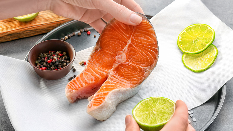 person drying and seasoning salmon filet on paper towel