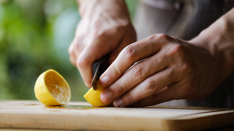 Hands slicing a lemon on a cutting board