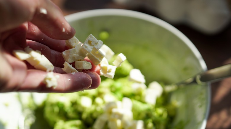 Person adding feta to avocado mash