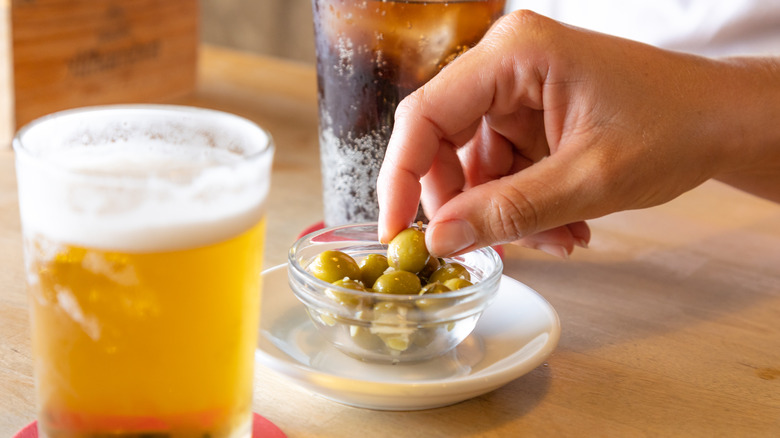 Hand plucks an olive from bowl beside beer