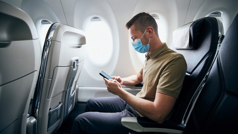 A masked man sits in an airplane seat