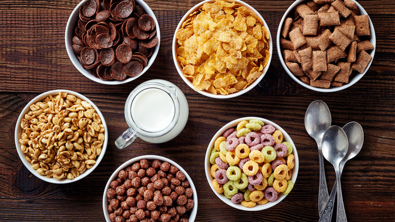 a variety of bowls of cereal with spoons and milk