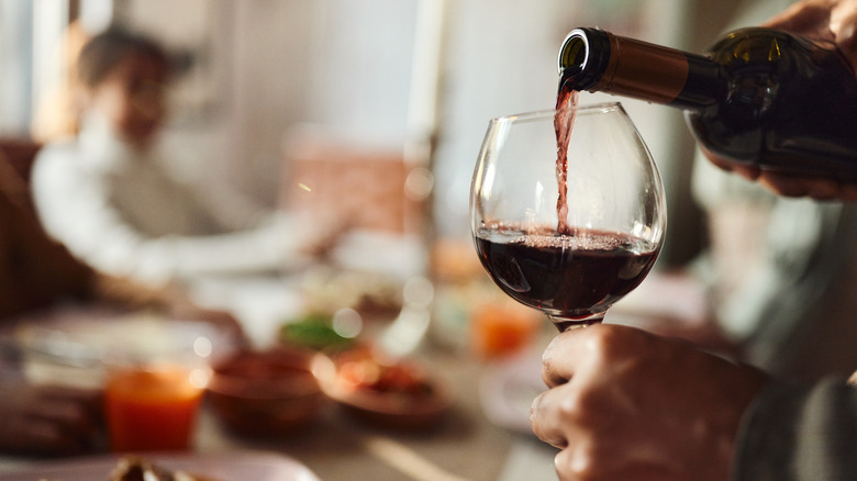 Person pouring a class of red wine next to a table