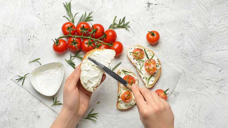 Spreading cream cheese on bread with tomatoes