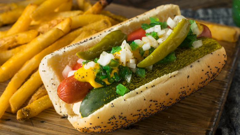 A Chicago-style hot dog on a serving plank with fries