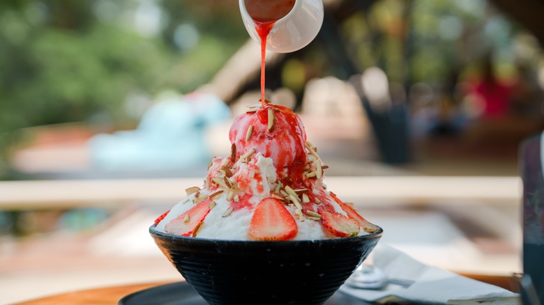 Pouring strawberry syrup over bowl of shaved ice