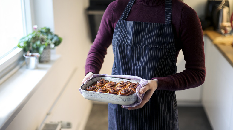 A woman holding a baking pan of cinnamon rolls