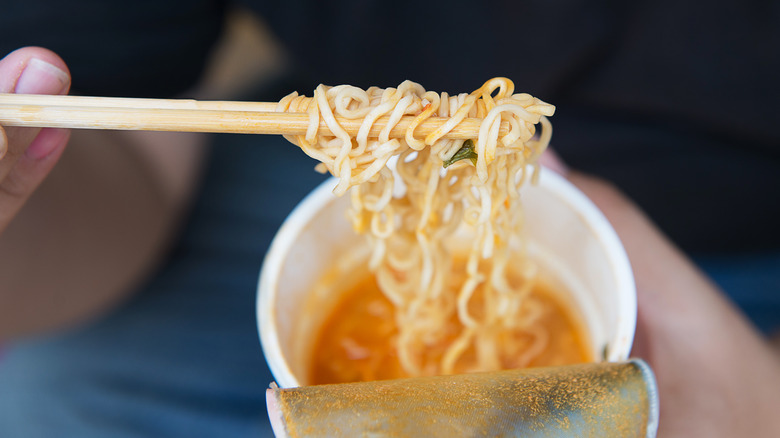 Cup noodles being held up by chopsticks