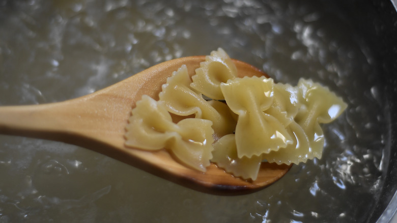 Wooden spoon hoding farfalle over boiling water