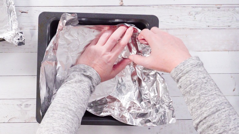 Person folding foil in pan