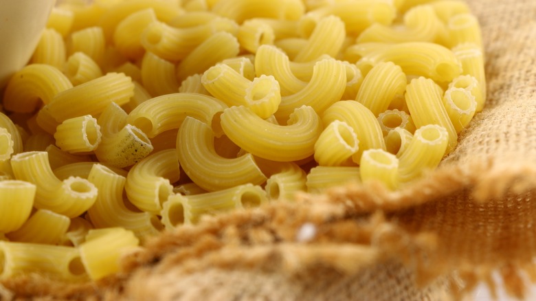 pile of uncooked elbow macaroni on burlap