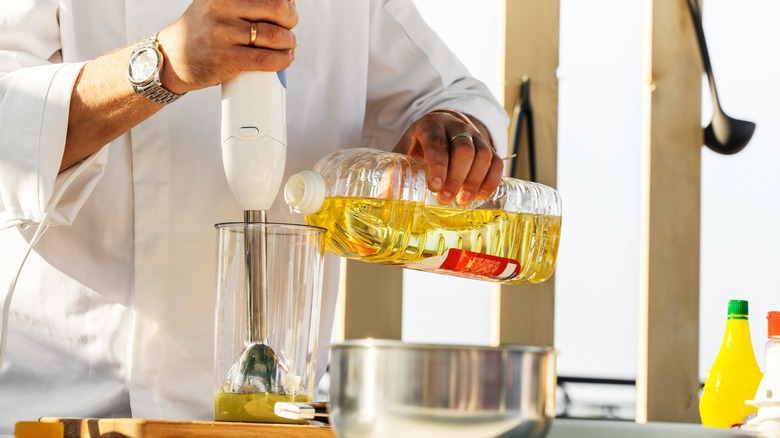 Hand pouring oil into container with immersion blender