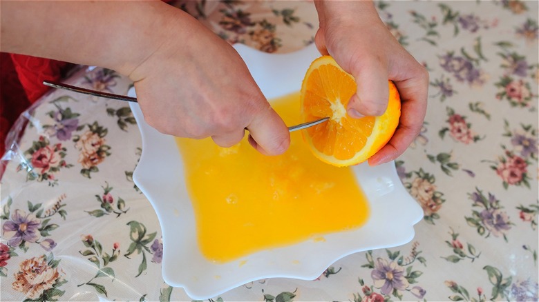 Squeezing orange over plate with fork 