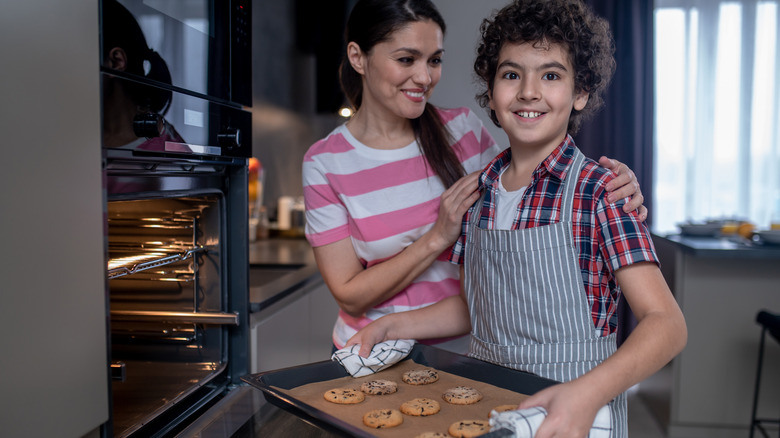 woman and child putting tray of chocolate chip cookies in the oven