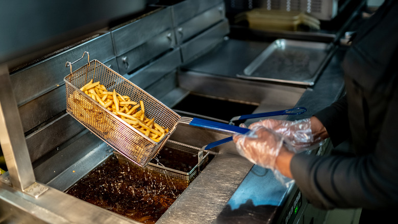 hand holds fryer with fries at fast food restaurant