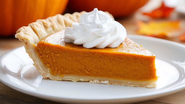 A slice of pumpkin pie on a dish with whipped cream on top.