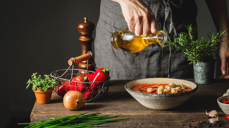 Person pouring oil over a bowl of soup on a rustic countertop