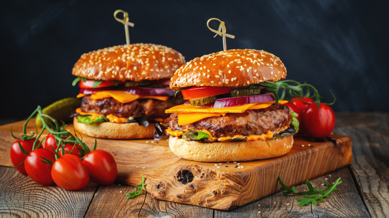 Two homemade burgers on a wood board with tomatoes