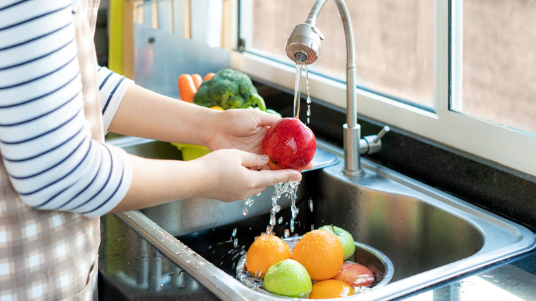 person washing fruit under a faucet