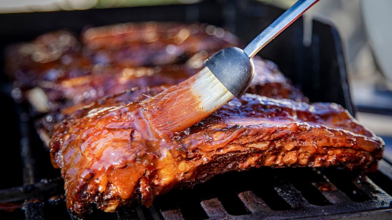 brushing BBQ sauce on grilled ribs