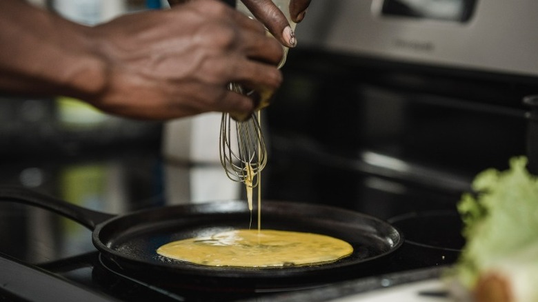 person pouring eggs on pan and whisk