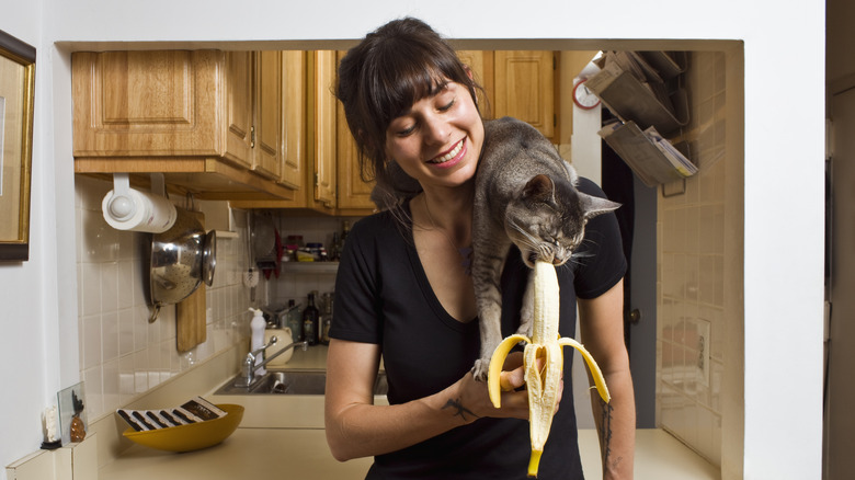 woman letting cat eat banana