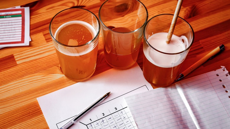 Three glasses of beer surround papers and pens