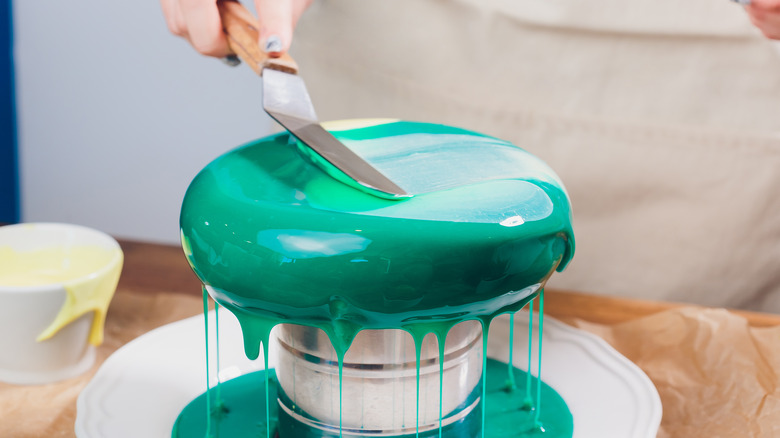 spreading green mirror glaze over a cake