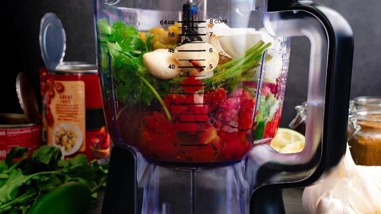 A food processor filled with tomatoes, cilantro, onions, garlic, and corn