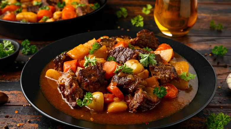 rich beef stew in a bowl with a glass of pale ale